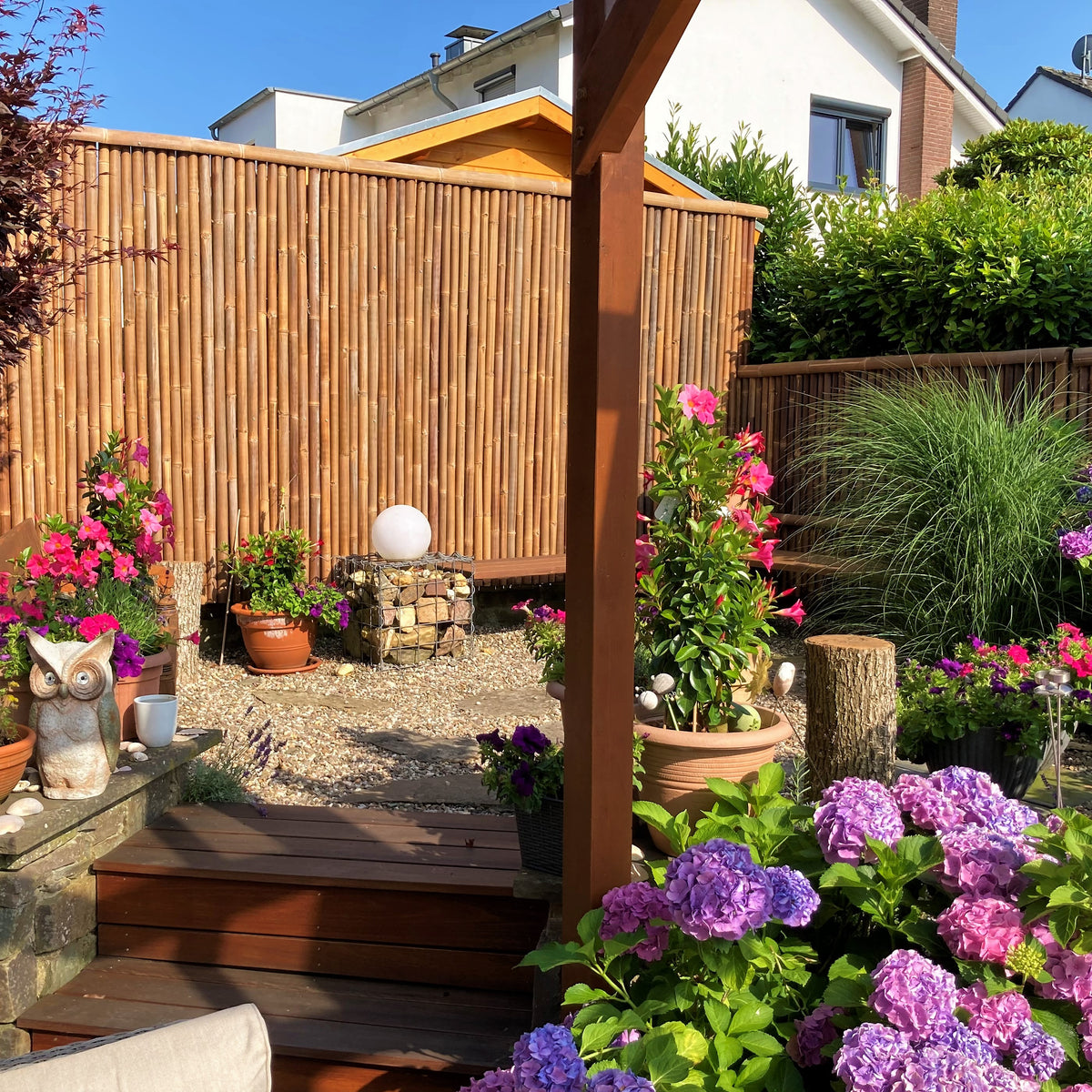 Blumiger Garten mit Rollmatte / Sichtschutz aus dunklem Bambus mit einem Dreiviertel-Bambusrohr als Zaunabdeckung