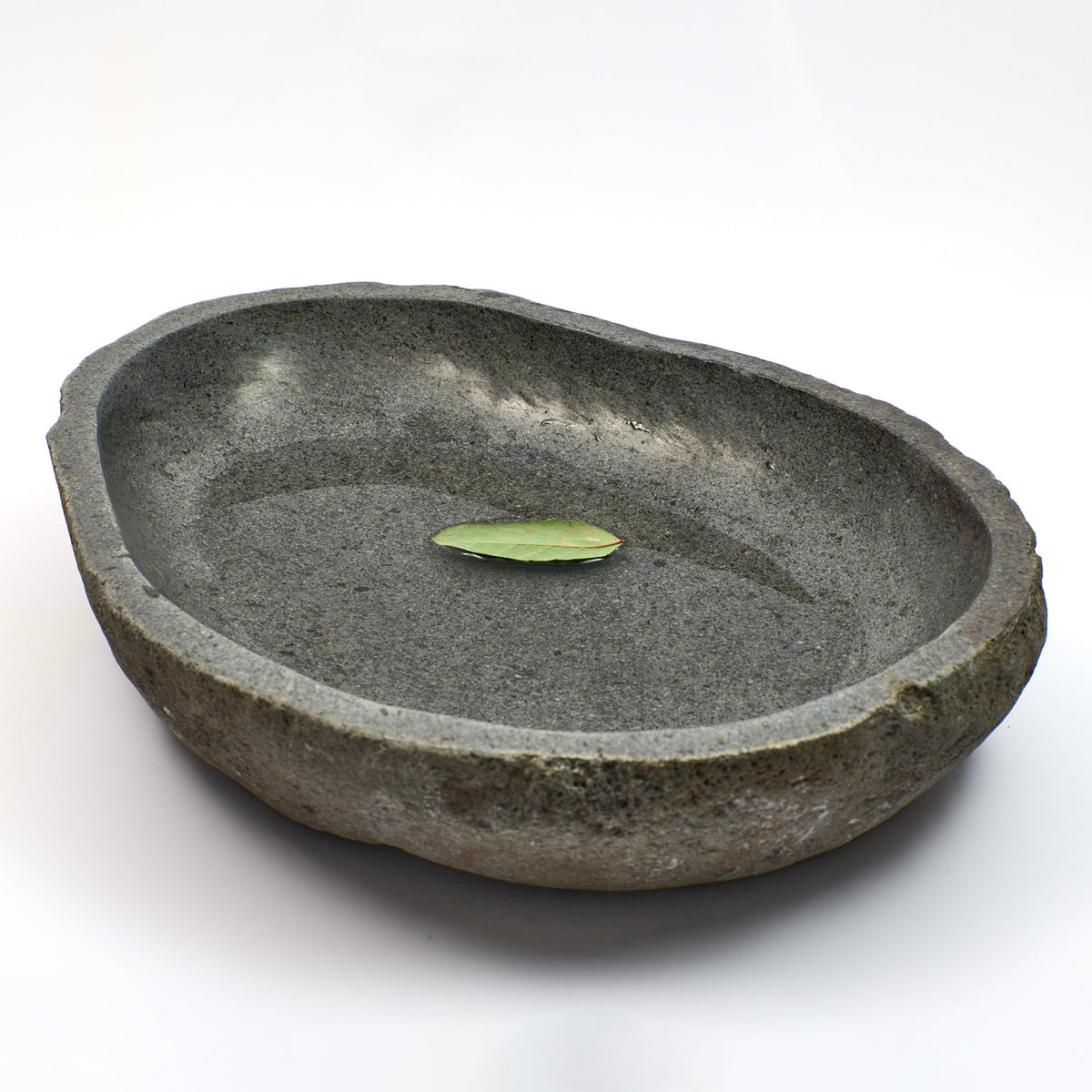Schale aus Flussstein mit grünem Blatt auf Wasseroberfläche