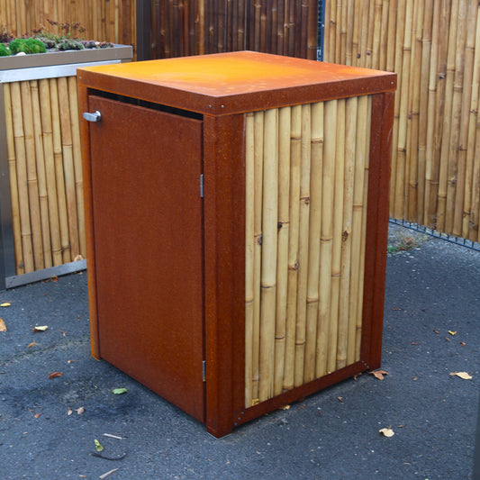 Mülltonnenbox mit Tür und Rahmen aus Cortenstahl, kombiniert mit hellen Bambusrohren, Frontansicht