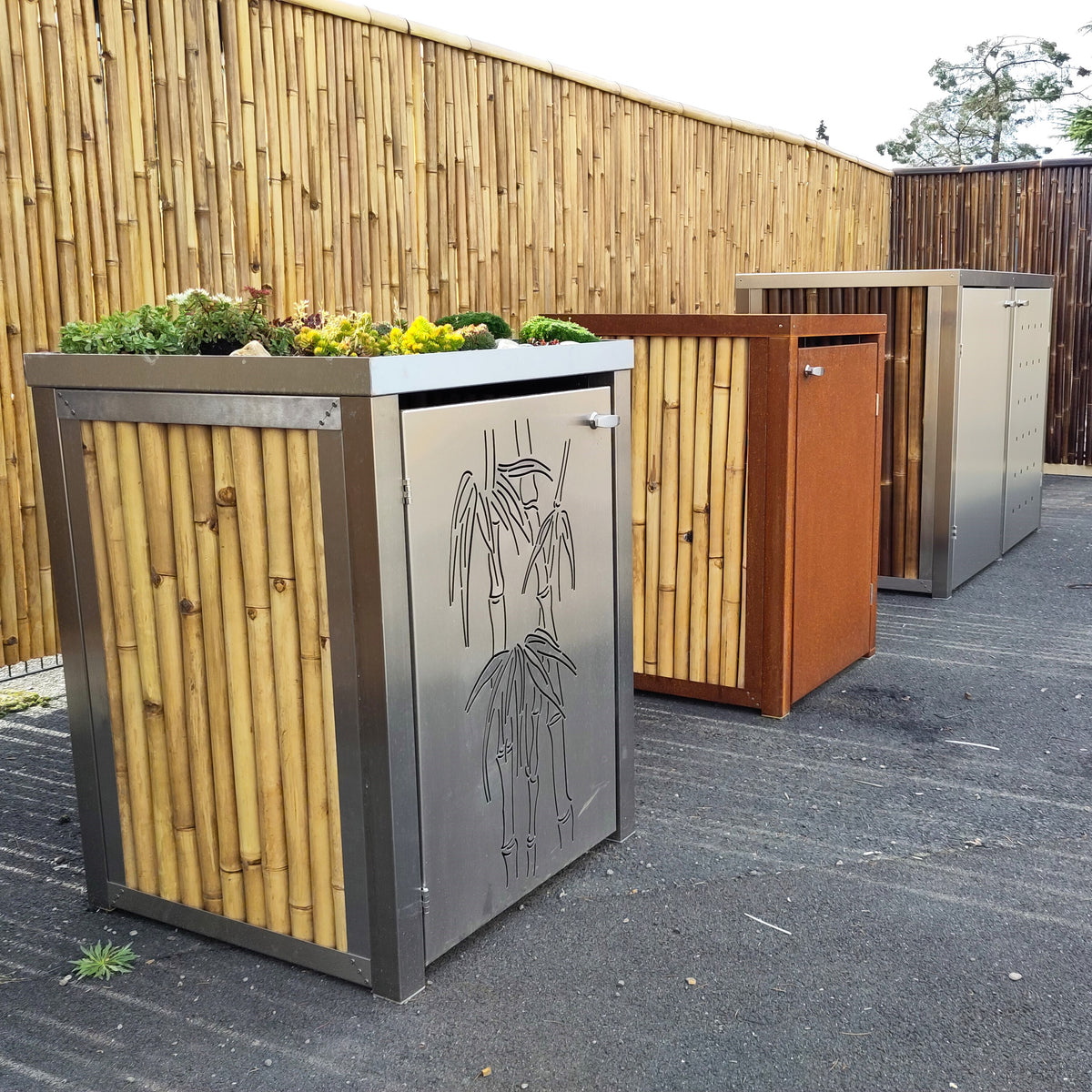 Mülltonnenbox mit Pflanzaufsatz, grauer Edelstahltür mit Bambusmotiv und Korpus aus Bambusrohren