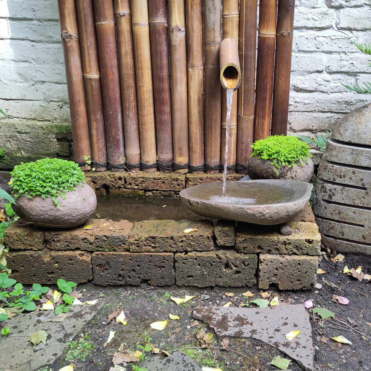 Bambus Wasserbrunnen mit bepflanzten Natursteintöpfen