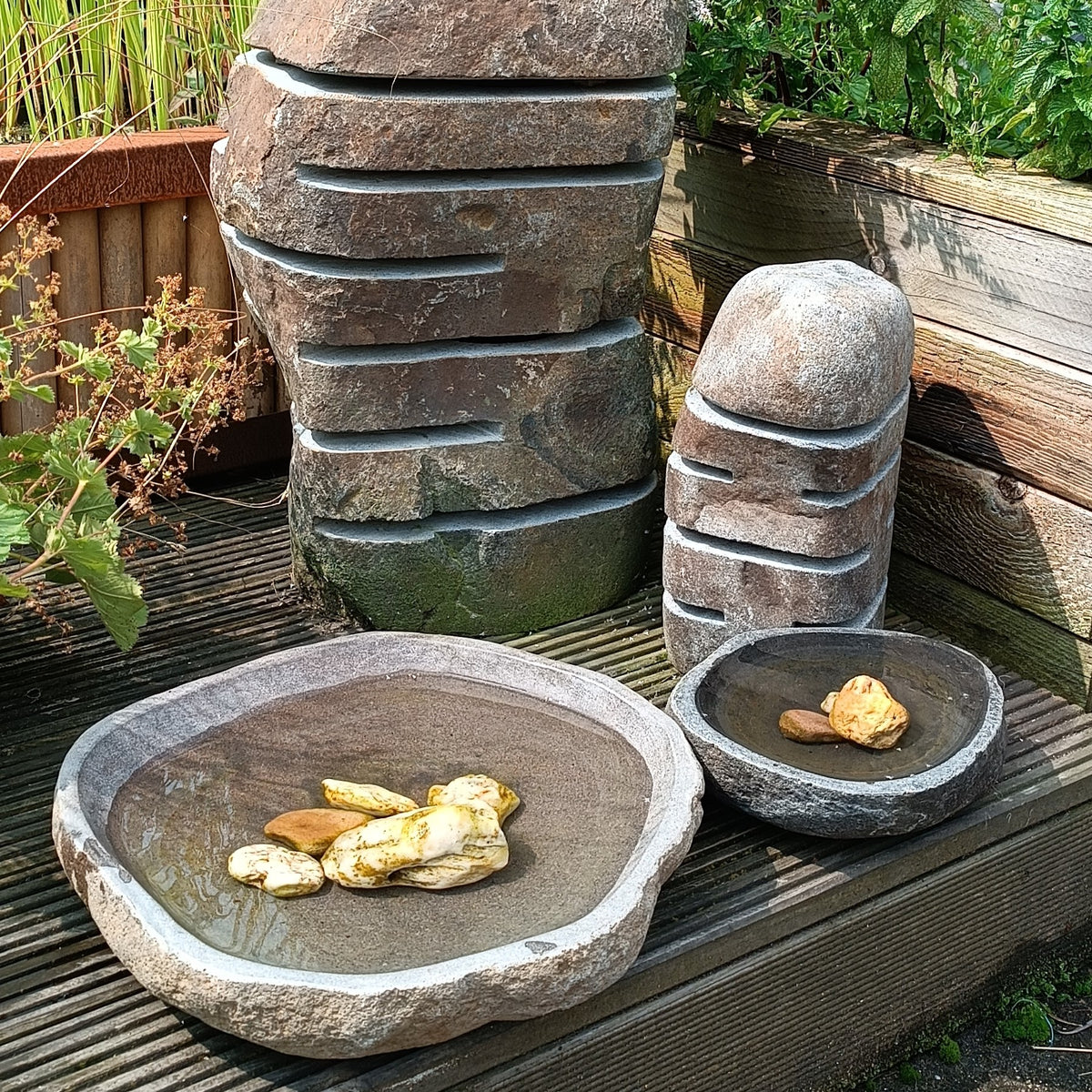 Schale aus Flussstein als Vogeltränke, runde graue Schalen auf Holzterrasse
